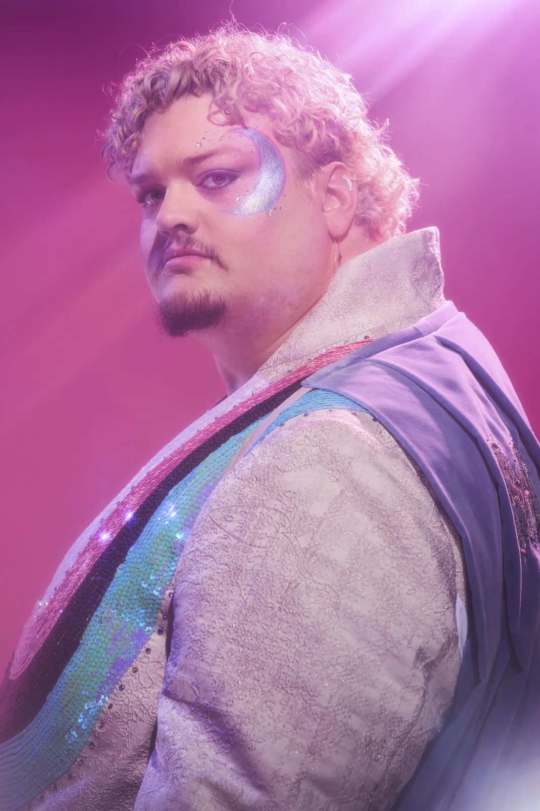 TALK in a shimmering stage costume under pink lighting.