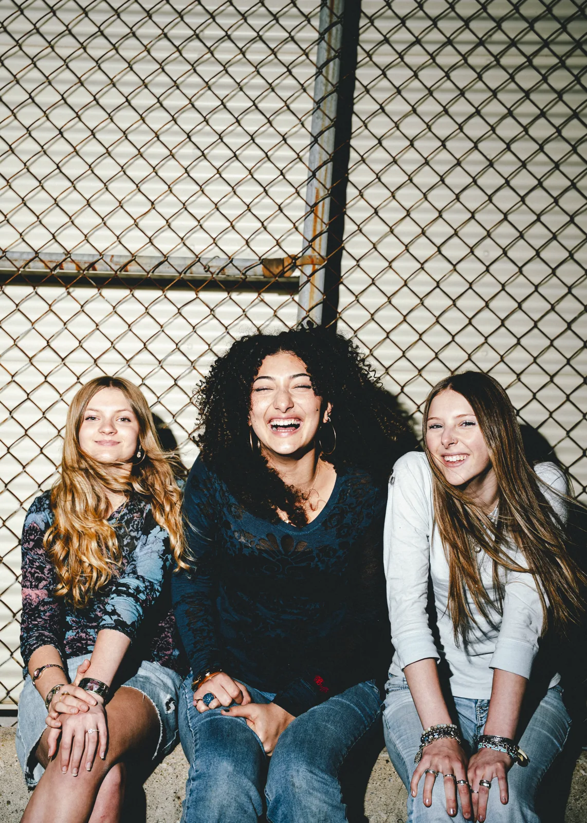 Thunder Queens laughing together beside a chain-link fence.
